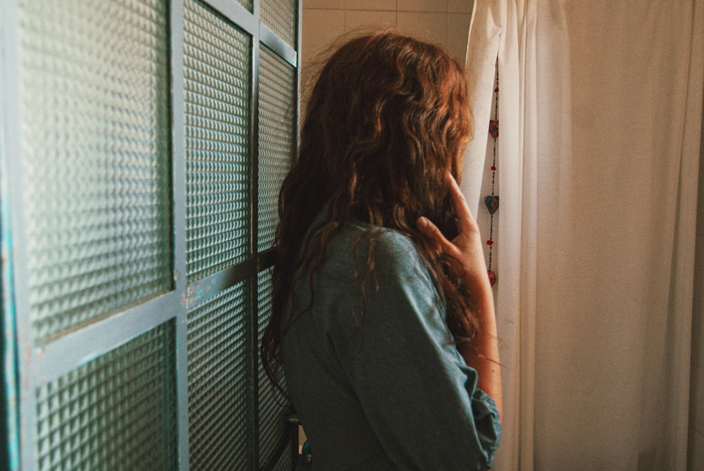 Frau in blauer Jeansjacke steht in der Nähe des Fensters