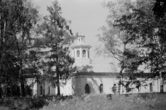 A vintage photo of the church's first building surrounded by trees.