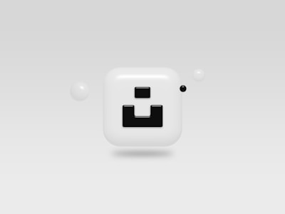 A glossy, rounded square icon with a bold black geometric design in the center, surrounded by small spherical objects on a minimalist gray background.