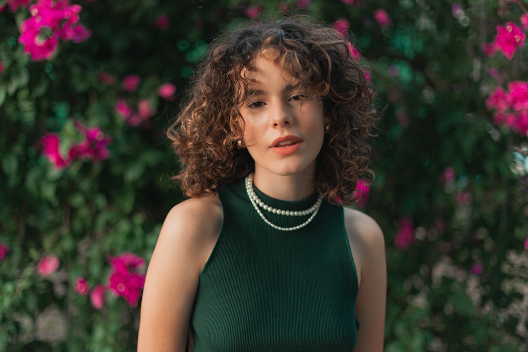 girl in green tank top standing near pink flower during daytime