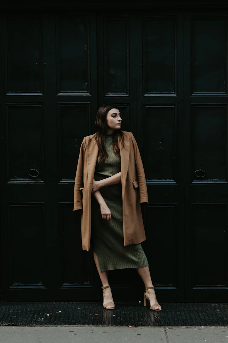 A woman in a brown coat standing beside a dark door
