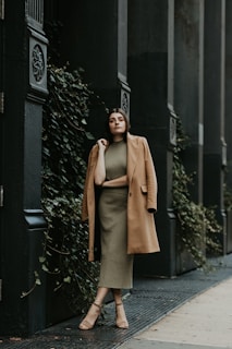 woman in brown coat standing near black metal gate during daytime