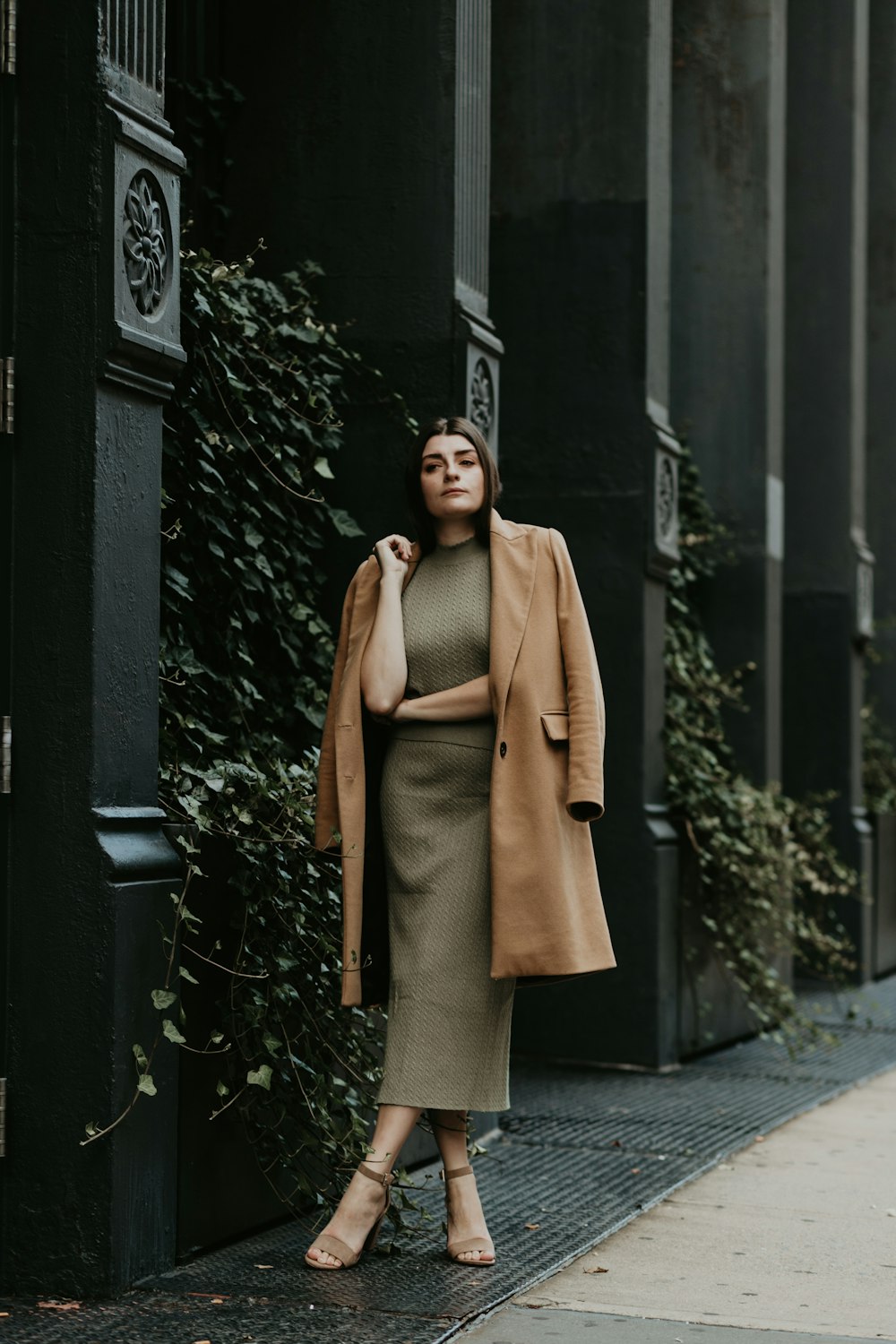 woman in brown coat standing near black metal gate during daytime