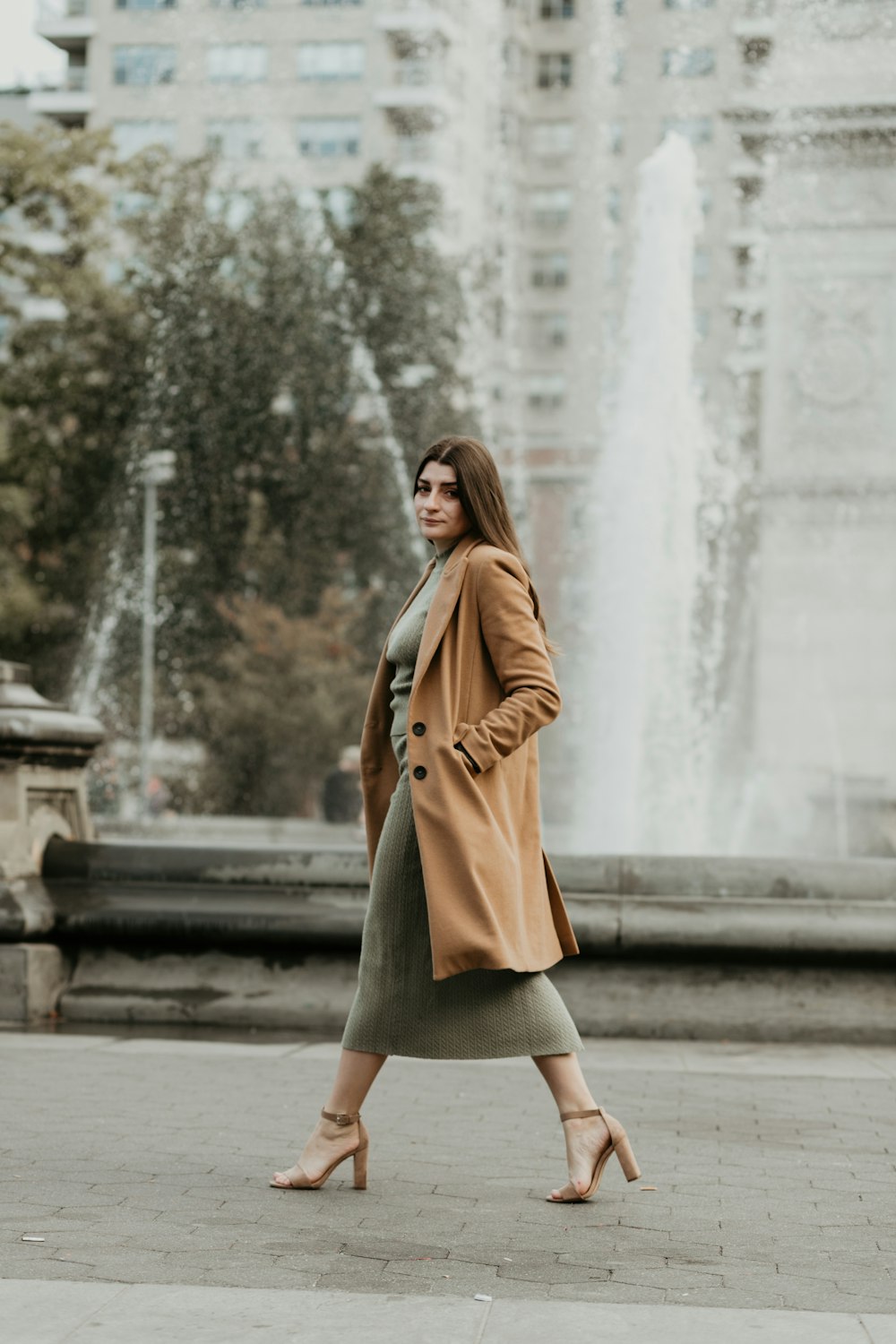 woman in brown coat standing on sidewalk during daytime