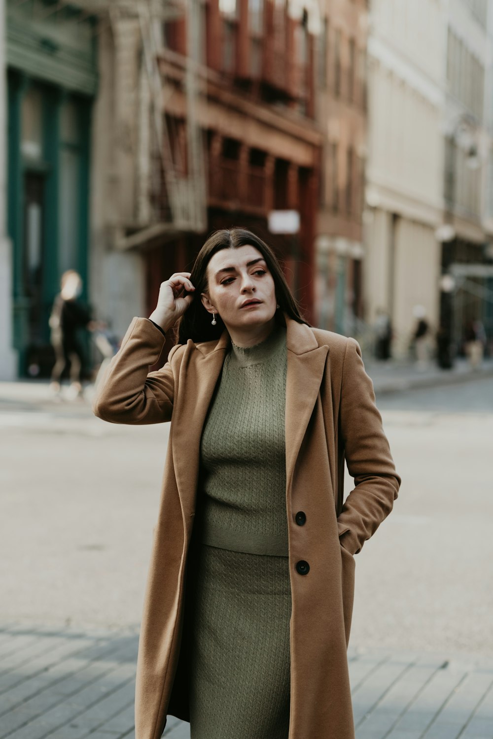 woman in brown coat standing on sidewalk during daytime