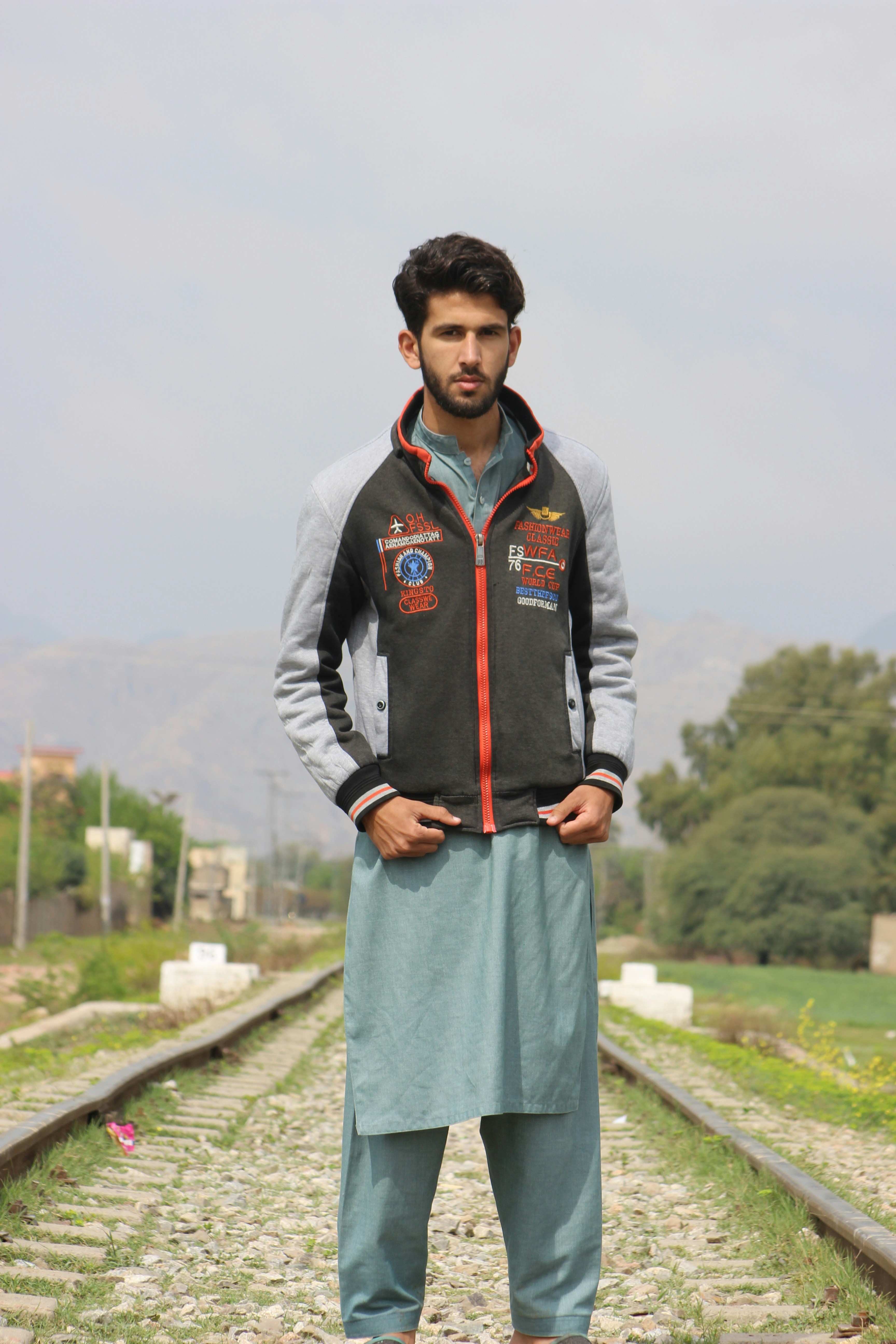 man in black leather jacket standing on gray concrete pathway during daytime