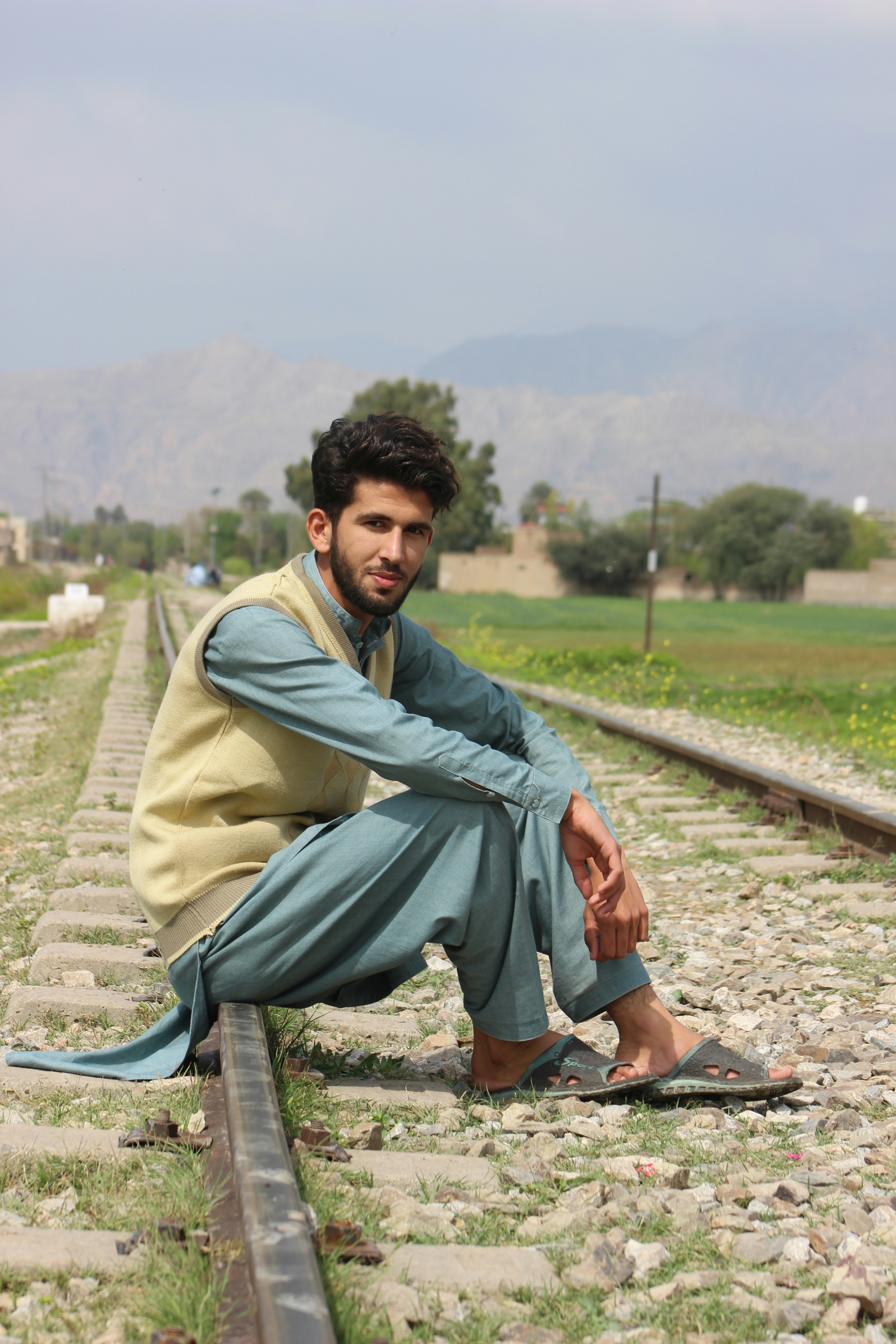 man in green and black jacket sitting on train rail during daytime