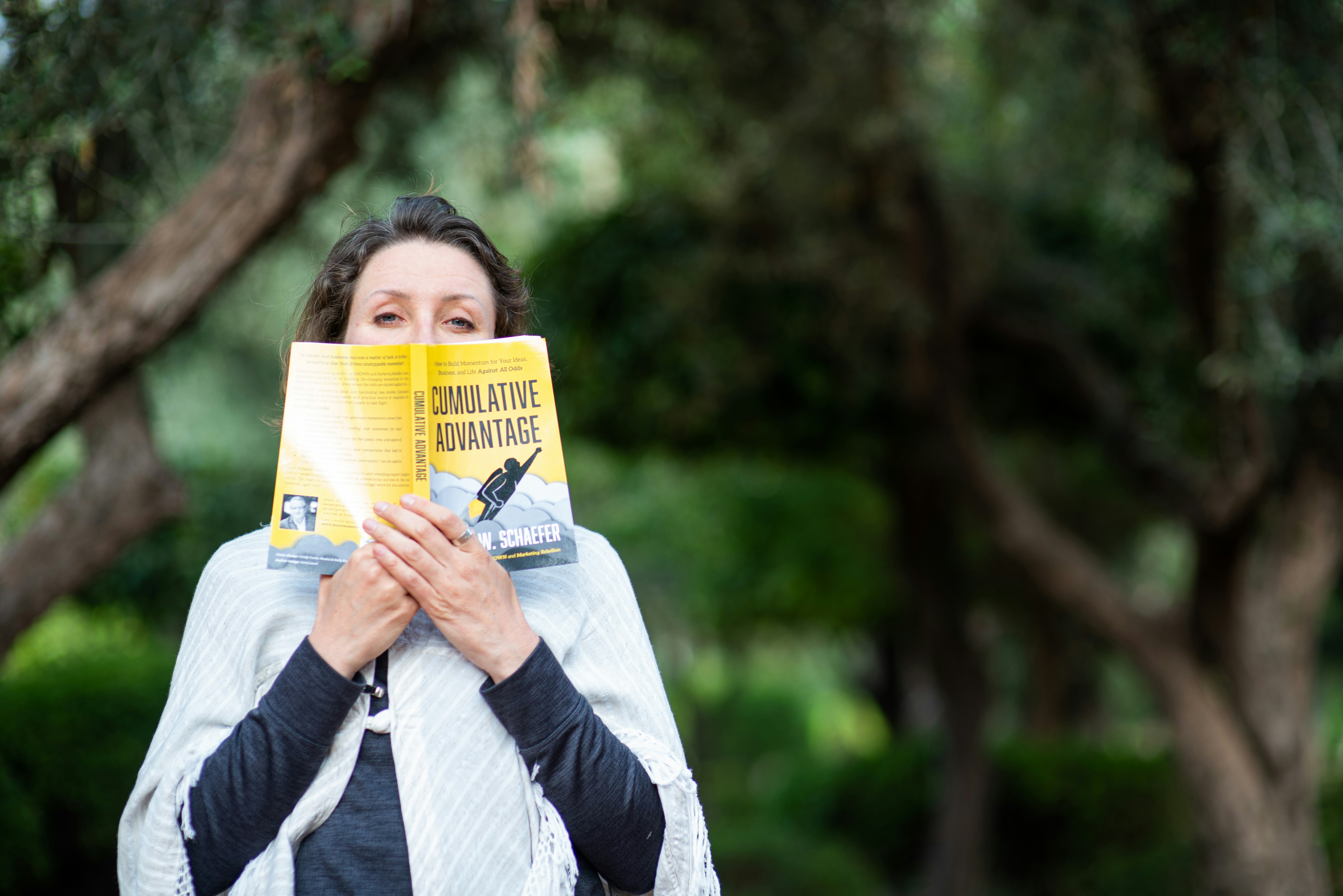 An excited woman reading a paperback book in the park, looking at camera