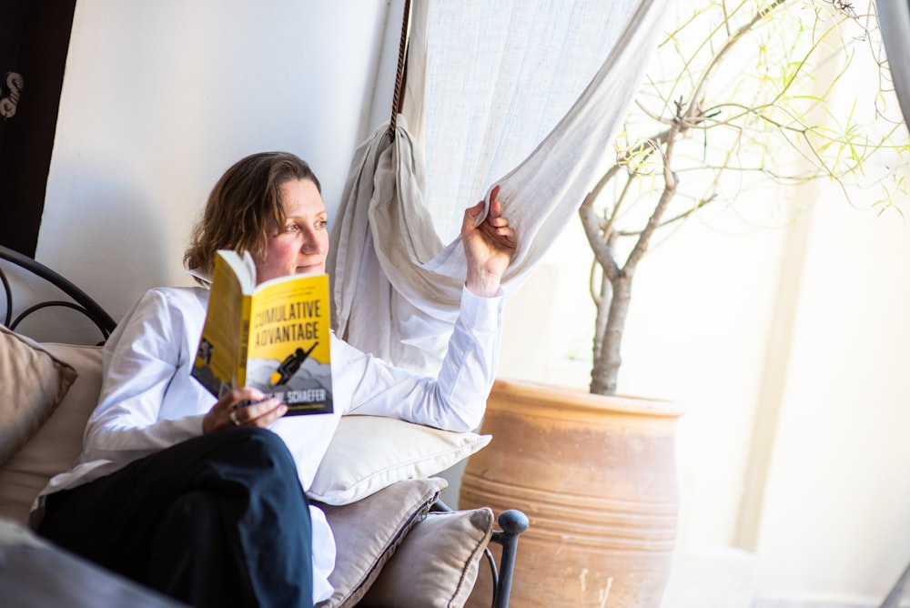 woman in white long sleeve shirt sitting on chair reading book