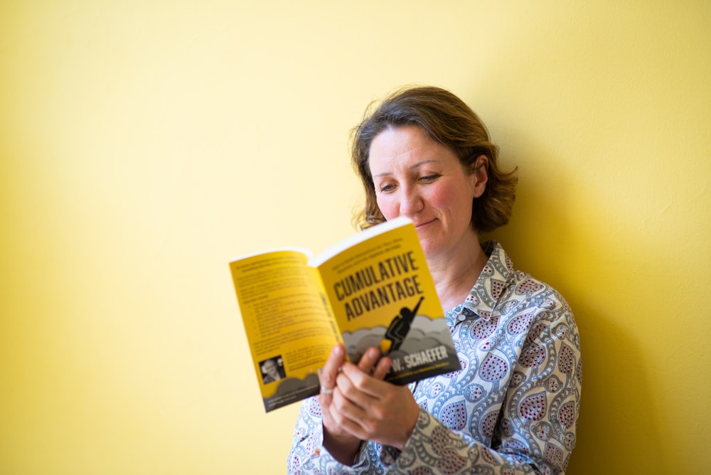 Mujer en camisa de manga larga floral blanca y azul sosteniendo un libro amarillo