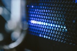A close-up view of a perforated metal surface with blue light shining through the small circular holes, creating an abstract and futuristic appearance.