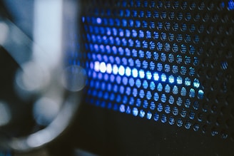 A close-up view of a perforated metal surface with blue light shining through the small circular holes, creating an abstract and futuristic appearance.