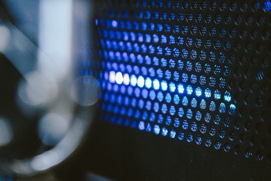 A close-up view of a perforated metal surface with blue light shining through the small circular holes, creating an abstract and futuristic appearance.