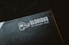 A close-up of a product packaging with the logo 'Glorious PC Gaming Race' printed in white on a dark background. The package features a stylized profile of a bearded face with flowing hair.