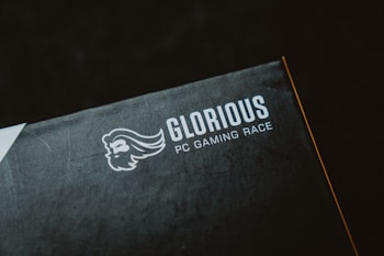 A close-up of a product packaging with the logo 'Glorious PC Gaming Race' printed in white on a dark background. The package features a stylized profile of a bearded face with flowing hair.