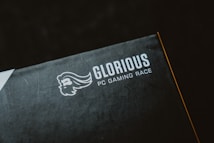 A close-up of a product packaging with the logo 'Glorious PC Gaming Race' printed in white on a dark background. The package features a stylized profile of a bearded face with flowing hair.