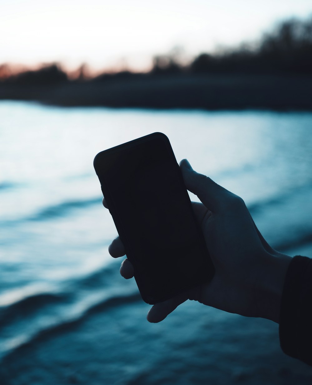 person holding black smartphone near body of water during daytime