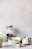 A cozy kitchen scene with a sage green ceramic bowl filled with fresh fruit on a linen cloth.