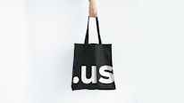 Close-up of a hand holding a brightly illustrated tote bag with smooth rounded typography.
