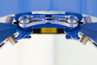 A close-up view of a metallic mechanical component, possibly part of a robotic or industrial apparatus, surrounded by structures in a blue hue. The metallic surface appears polished with screws and rounded edges visible. The background is out of focus, contributing to the central focus on the mechanical part.