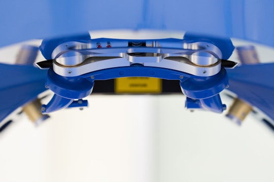 A close-up view of a metallic mechanical component, possibly part of a robotic or industrial apparatus, surrounded by structures in a blue hue. The metallic surface appears polished with screws and rounded edges visible. The background is out of focus, contributing to the central focus on the mechanical part.