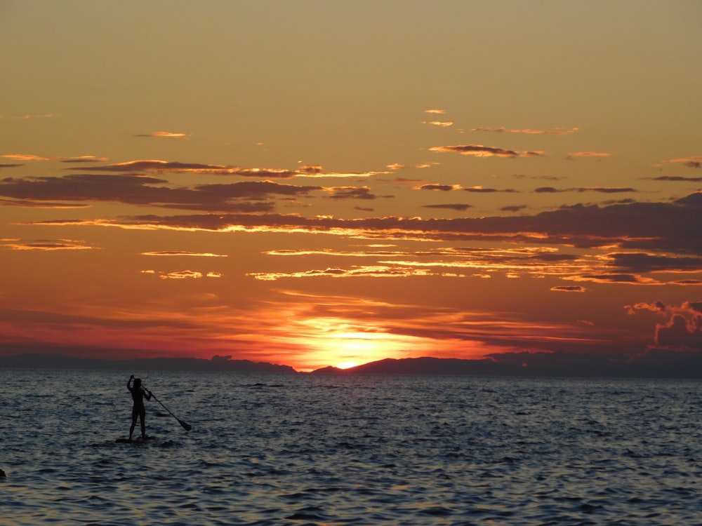 silhouette of man standing on sea shore during sunset