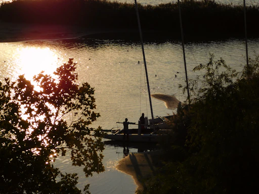 Golden hour light casting warm hues over a sailboat gently rocking on calm water, with a couple laughing on deck.
