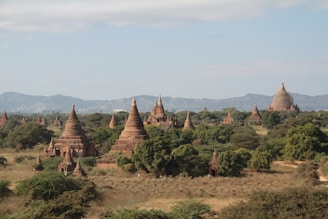 A vast, ancient landscape filled with numerous pagodas and temples, surrounded by lush greenery and hills in the distance. The structures have distinct, spire-like roofs, characteristic of traditional Southeast Asian architecture. The scene is serene and expansive with a clear sky above.