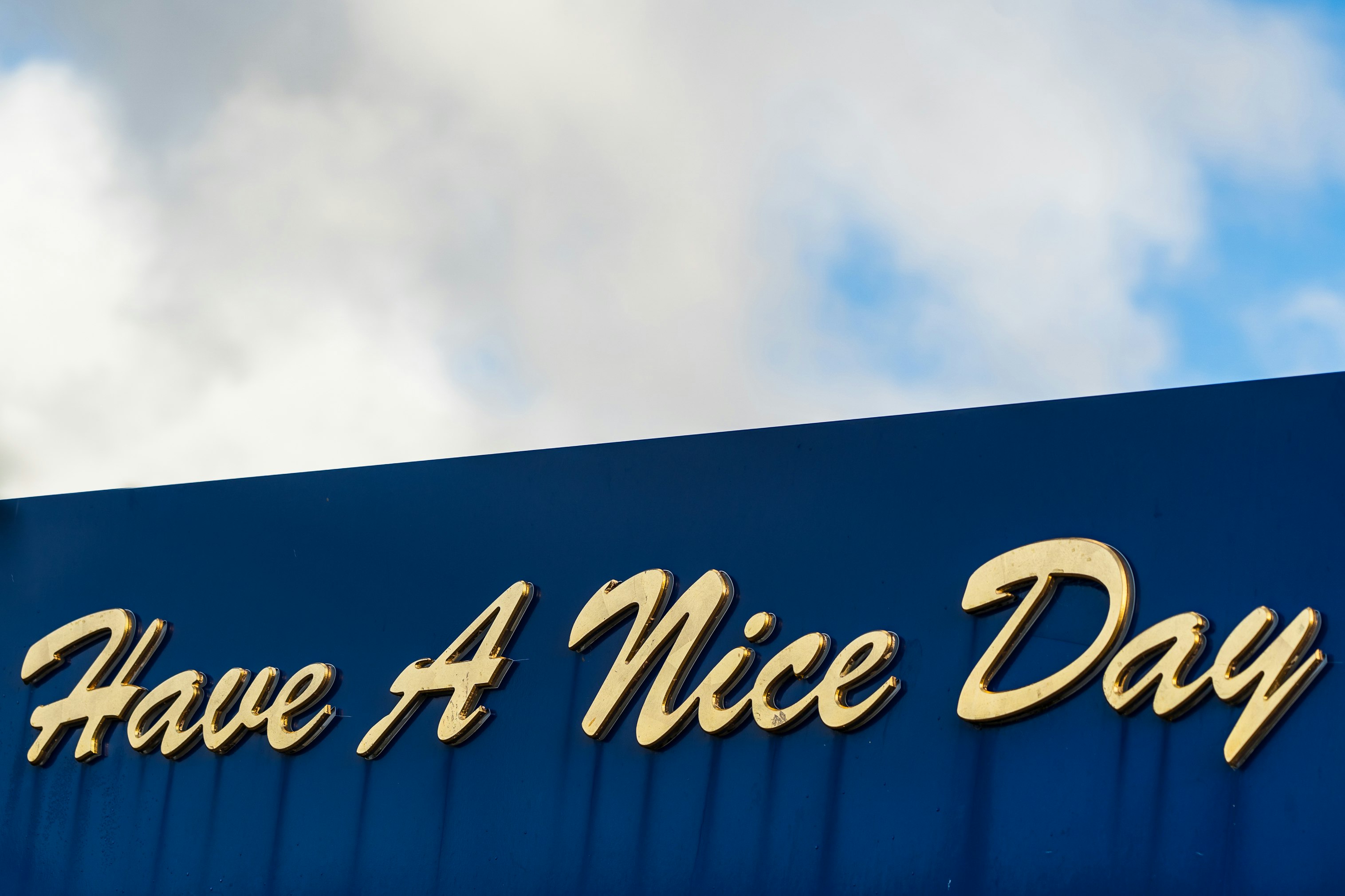 A sign saying Have A Nice Day, outside a cafe, with gold lettering on a blue background.