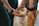 A person gently petting a dog on its head with both hands. The dog appears calm and attentive, looking slightly upwards. The background is blurred, focusing the viewer's attention on the interaction between the person and the dog.
