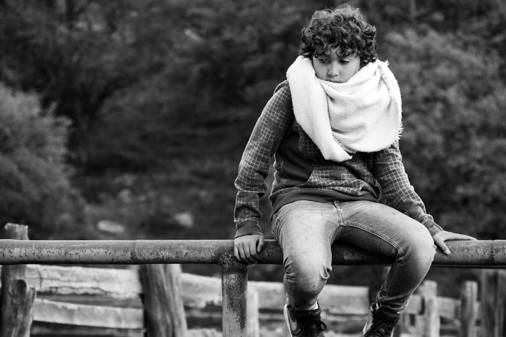 grayscale photo of woman sitting on wooden fence