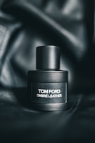 A sleek, matte black perfume bottle labeled with the text 'Tom Ford Ombré Leather' sits on a dark, textured background that enhances its luxurious appearance.