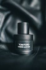 A sleek, matte black perfume bottle labeled with the text 'Tom Ford Ombré Leather' sits on a dark, textured background that enhances its luxurious appearance.