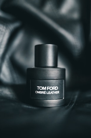 A sleek, matte black perfume bottle labeled with the text 'Tom Ford Ombré Leather' sits on a dark, textured background that enhances its luxurious appearance.