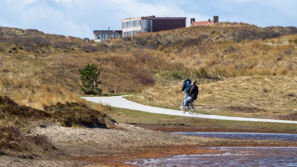 man in black jacket and blue denim jeans riding bicycle on road during daytime