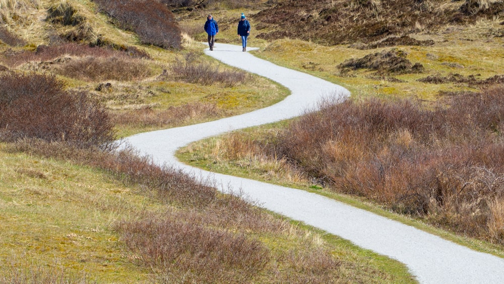 2 people walking on pathway between green grass field during daytime