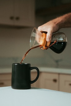 person pouring coffee on black ceramic mug