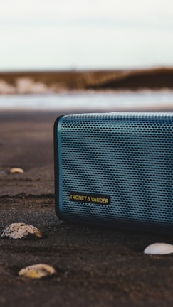 black and gray jbl portable speaker on gray sand during daytime
