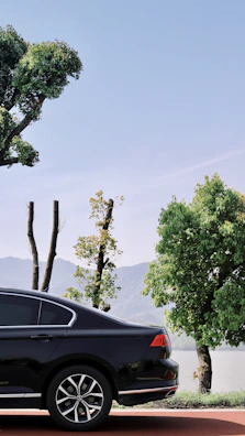 A sleek car parked beside a crystal-clear lake reflecting surrounding pine trees.