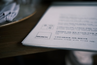 A close-up of a menu on a wooden table, featuring dishes in both English and Chinese. The section titled 'BRUNCH' is highlighted, with some items partially visible.