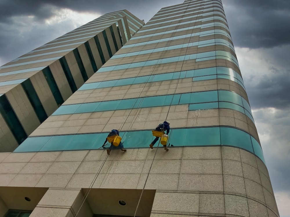 Hombre con camisa amarilla y jeans de mezclilla azul sentado en un edificio de concreto gris durante el día