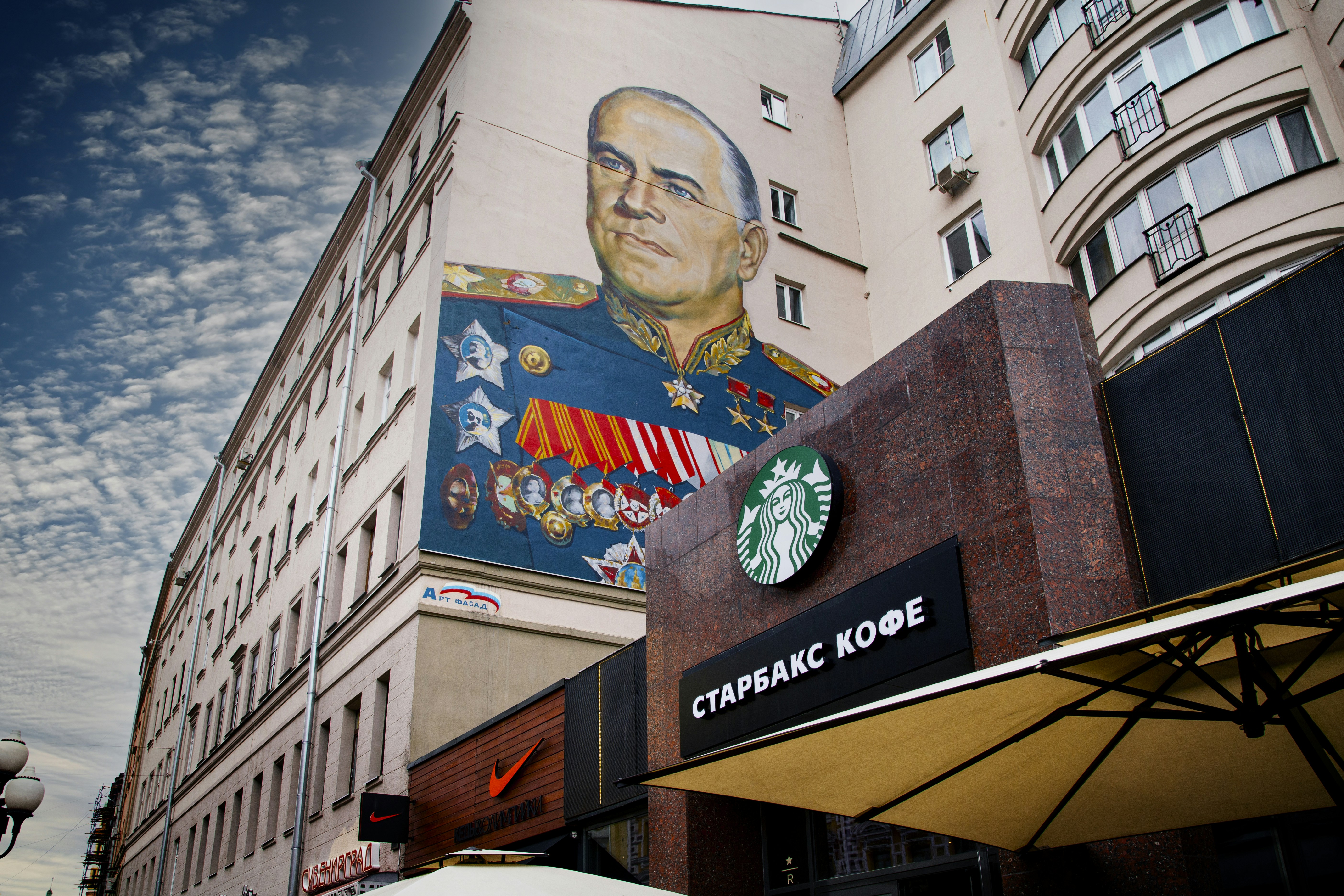uomo in occhiali da vista con montatura nera e giacca nera in piedi davanti all'edificio in cemento marrone durante