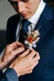 An elegant boutonniere with tiny white blooms and greenery pinned on a navy suit lapel.