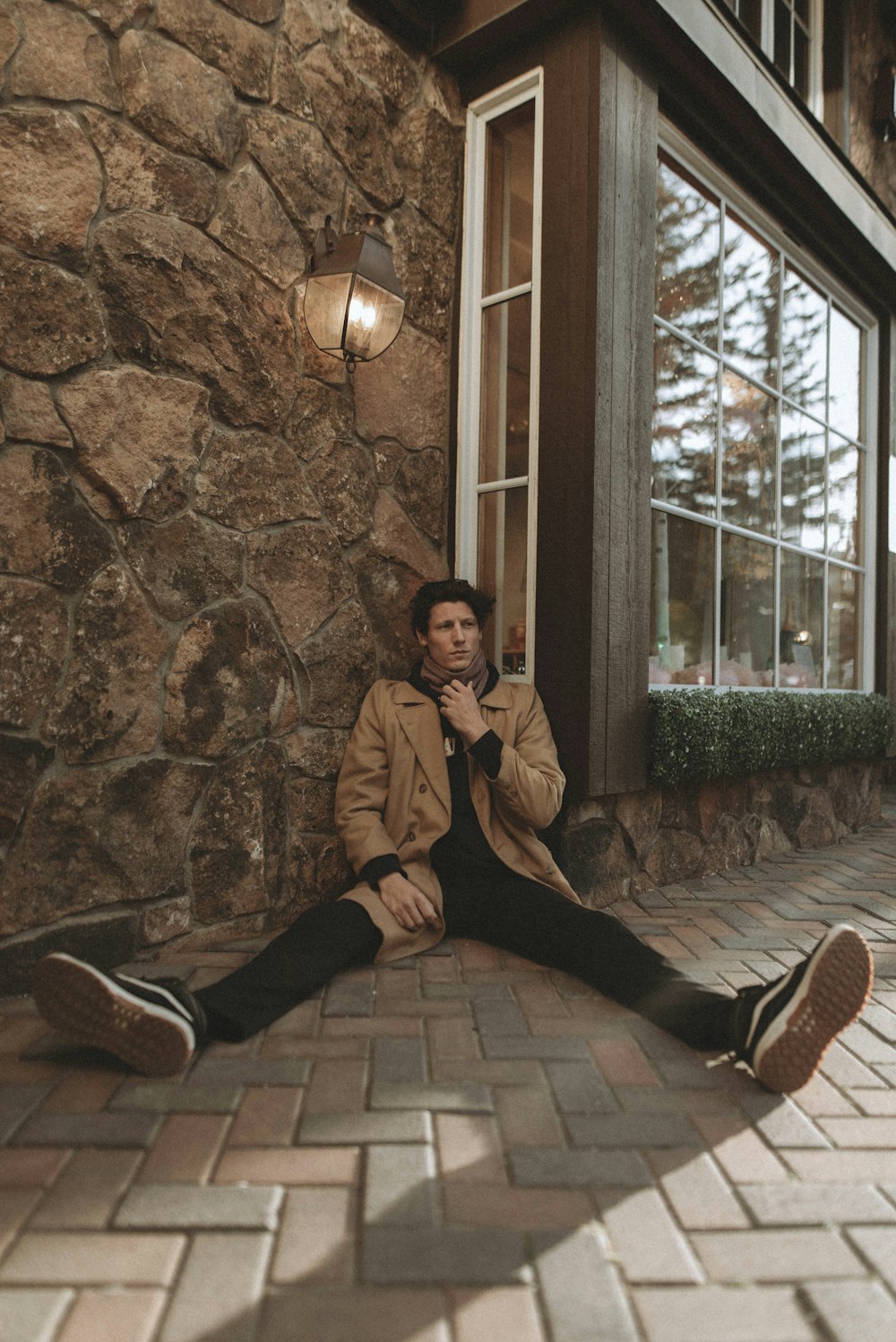 man in brown jacket and black pants sitting on brown concrete wall