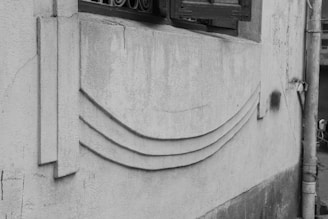 A textured concrete wall with decorative geometric patterns, featuring three curved lines and a vertical panel. A small window with a metal grill and an electrical pipe are visible.