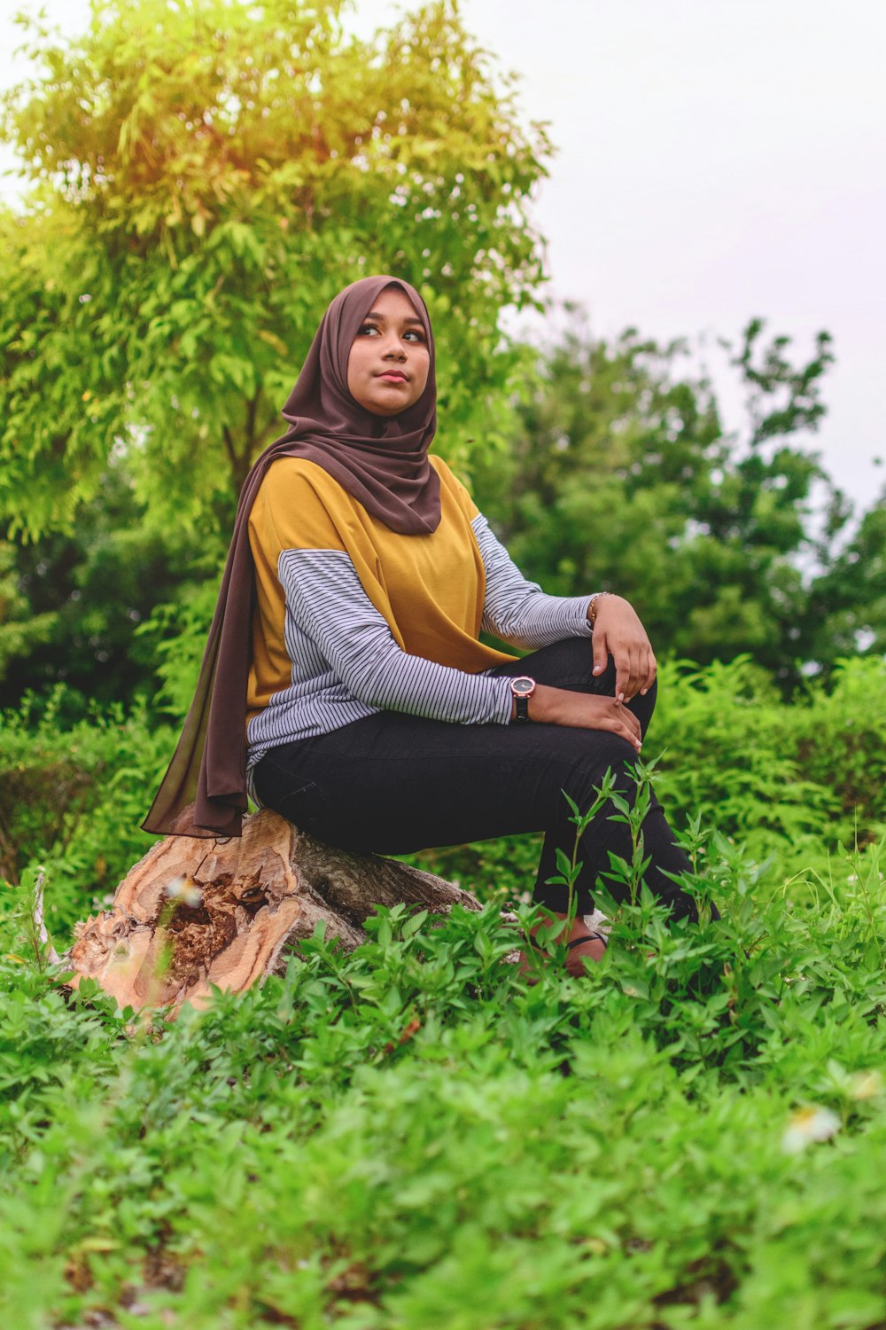 茶色の丸太に座る黄色いヒジャブの女性
