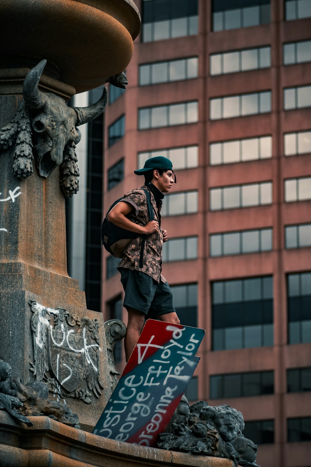 Hombre con camisa blanca y negra y pantalones negros de pie junto a la estatua de hormigón gris