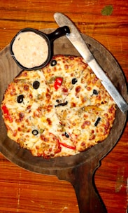 A rustic wooden board displaying both Roman pizza slices and a small bowl of dipping sauce.