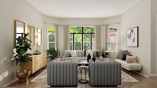A well-furnished living room with a modern, minimalist aesthetic. The space features a large window framed by light curtains, allowing natural light to flood the room. There is a gray tufted sofa set, a wooden sideboard, several potted plants, and a large framed artwork on the wall. The color palette is neutral with green and wooden accents.
