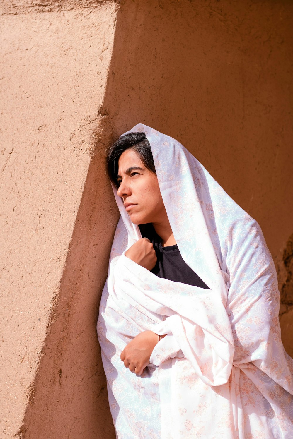 woman in white hijab leaning on brown wall